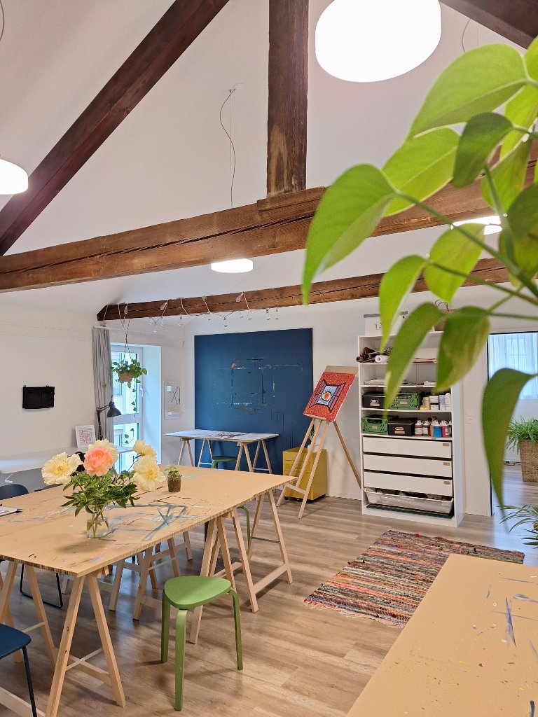 Heller Praxisraum mit rustikalen Holzbalken, grosser Arbeitstisch mit Blumen und kreativen Materialien, Einblick in die Praxis witErgo in Thun
