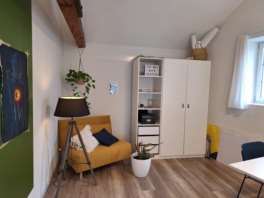 Gemütliche Ecke der Praxis mit gelber Sitzbank, Pflanzen und Regal, warme, einladende Atmosphäre bei witErgo